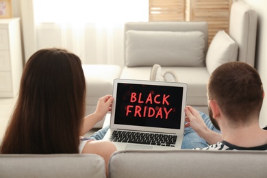 Photo of Couple using laptop with Black Friday announcement on screen at home