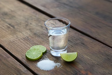Photo of Mexican tequila shot with lime slices and salt on wooden table. Drink made from agave