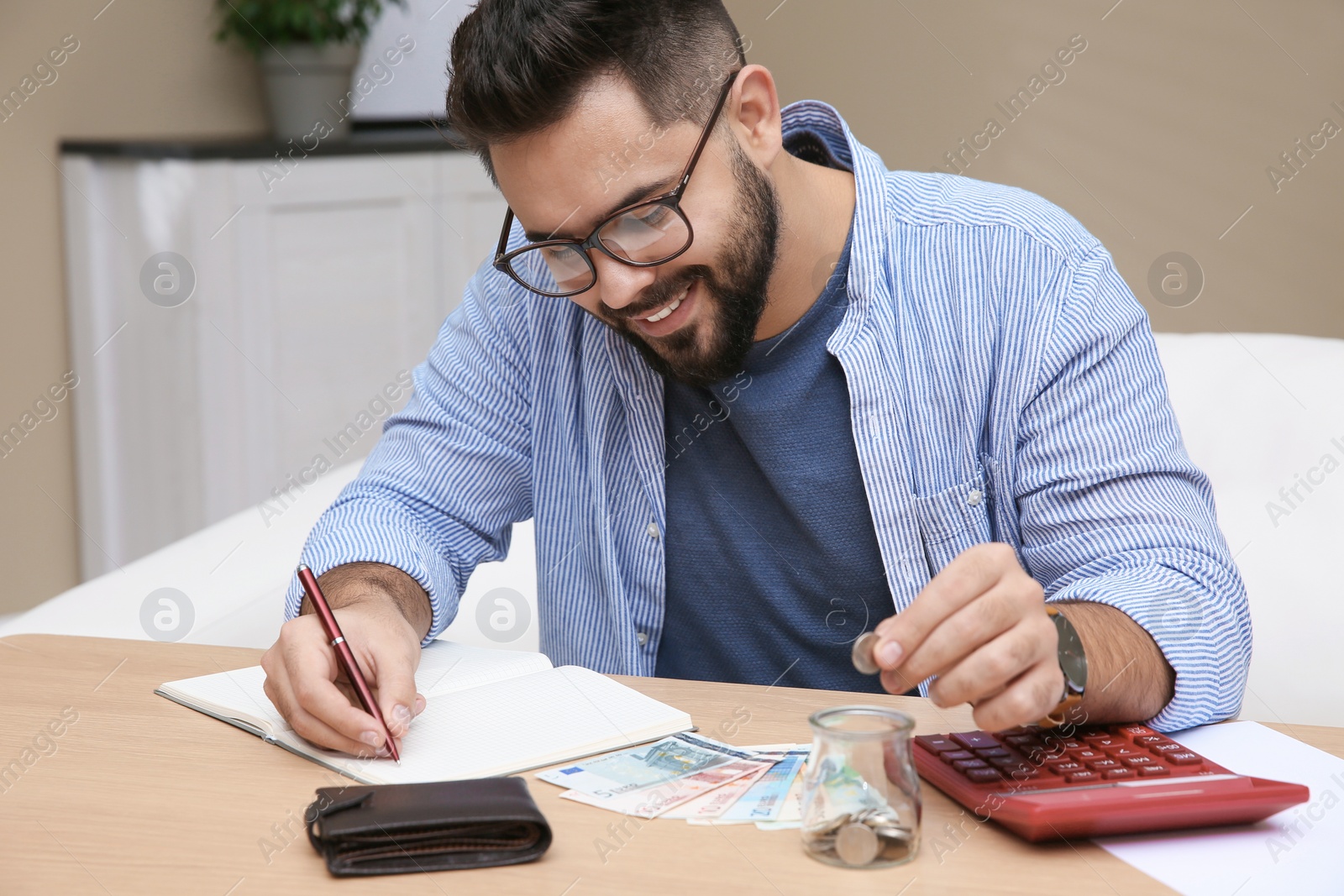 Photo of Young man putting coin into glass jar at table indoors. Money savings