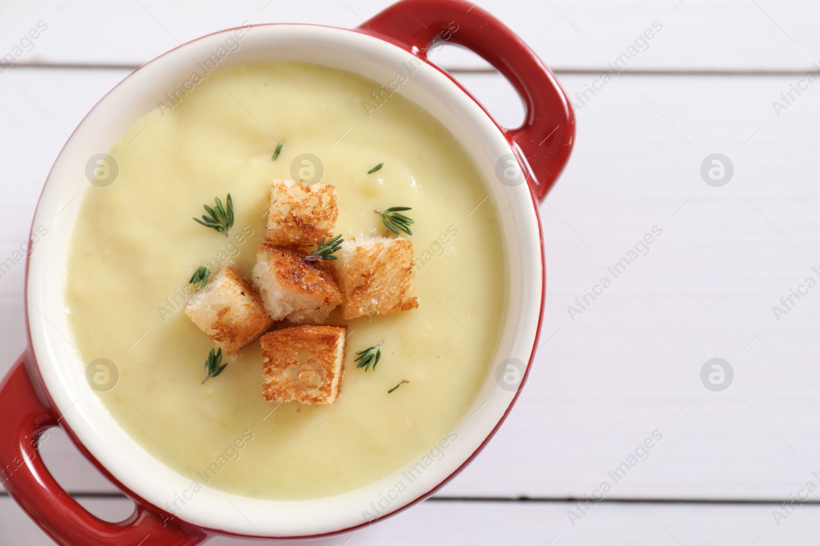 Photo of Tasty potato soup with croutons and rosemary in ceramic pot on white wooden table, top view. Space for text