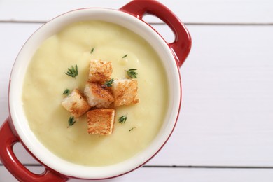 Photo of Tasty potato soup with croutons and rosemary in ceramic pot on white wooden table, top view. Space for text