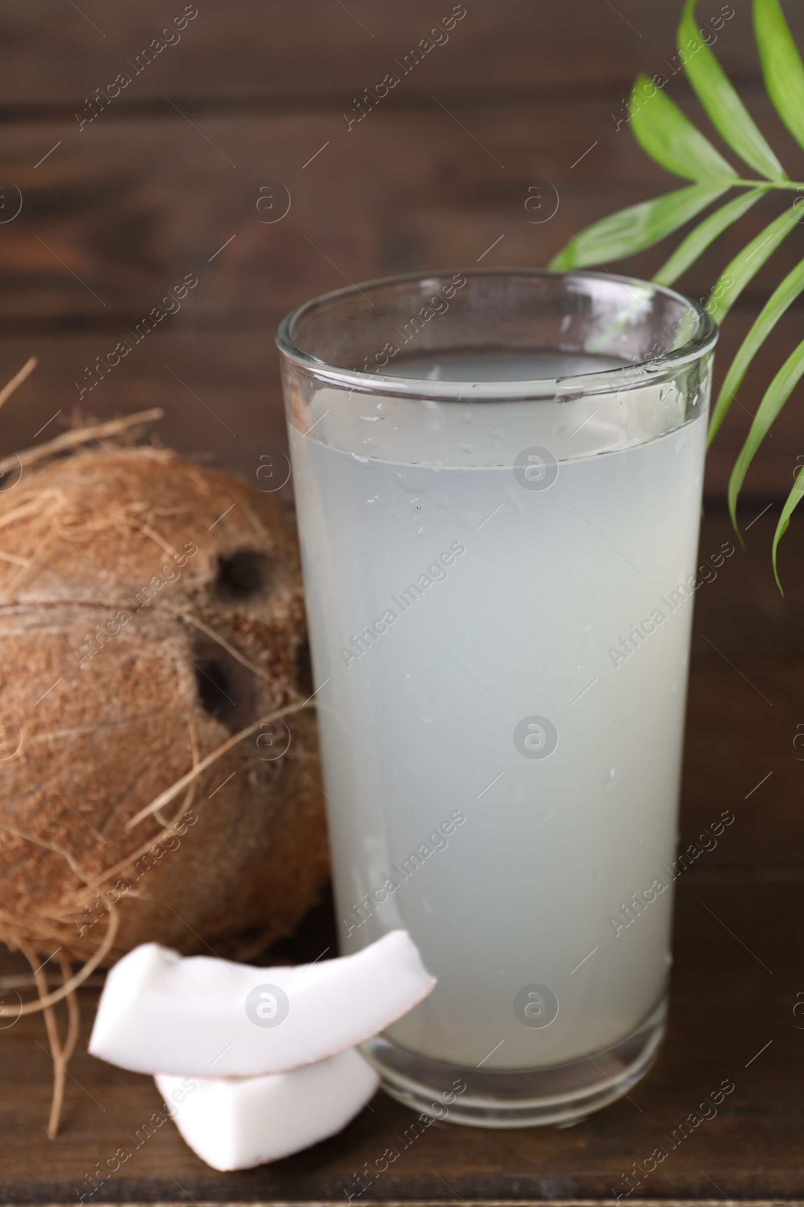 Photo of Glass of coconut water, leaf and nuts on wooden table