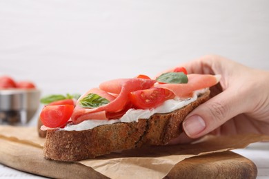 Photo of Woman taking tasty bruschetta with prosciutto, tomatoes and cheese from wooden board, closeup