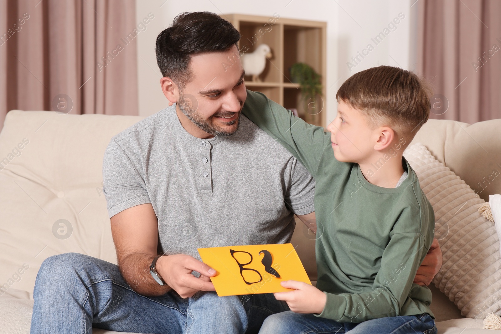 Photo of Cute little boy presenting his father with gift on sofa at home