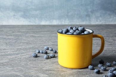 Photo of Fresh blueberries in yellow cup on color table. Space for text