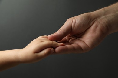 Father and child holding hands on dark grey background, closeup