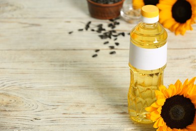 Photo of Sunflower cooking oil and yellow flowers on white wooden table, space for text