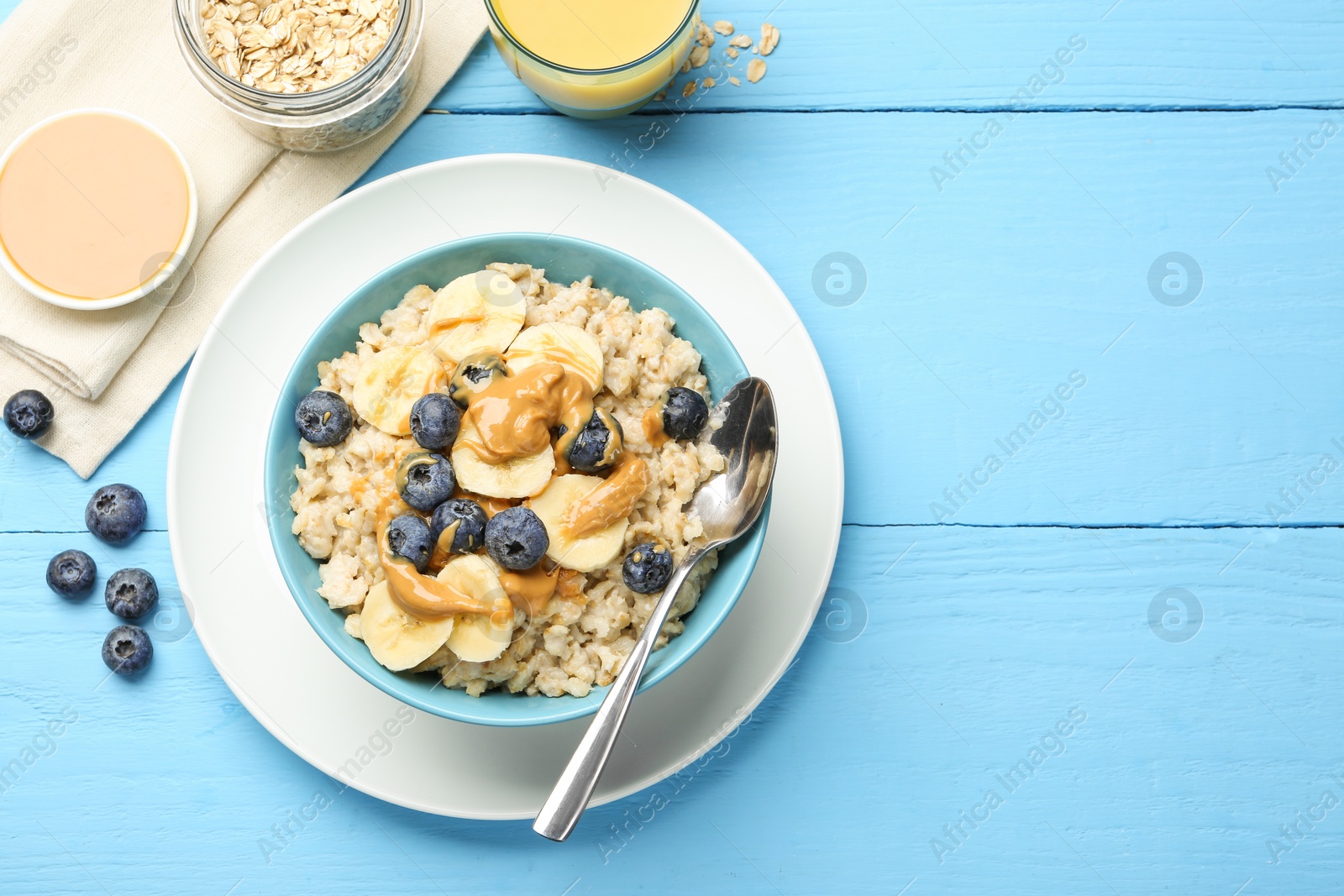 Photo of Tasty oatmeal with banana, blueberries and peanut butter served in bowl on light blue wooden table, flat lay. Space for text