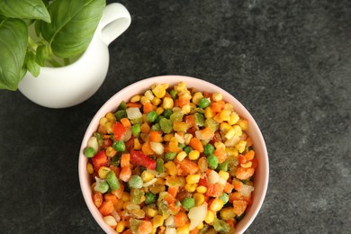 Photo of Mix of different frozen vegetables in bowl and basil on gray table, flat lay