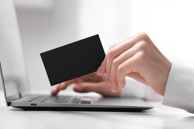 Photo of Woman with laptop holding blank business card at white table, closeup. Space for text