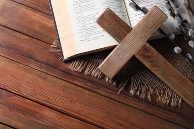 Photo of Cross, Bible and willow branches on wooden table, flat lay. Space for text