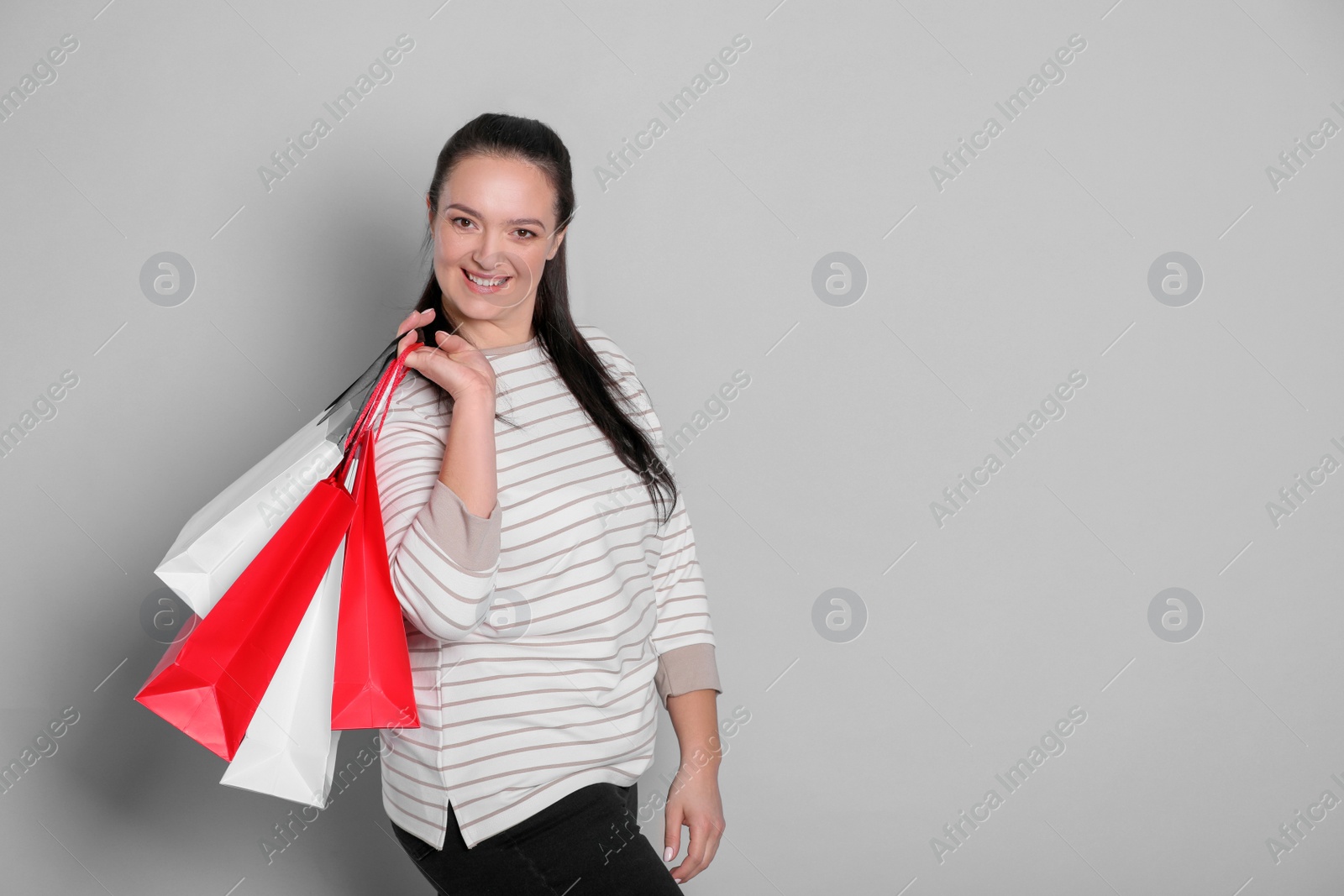 Photo of Beautiful overweight woman with shopping bags on light grey background. Space for text