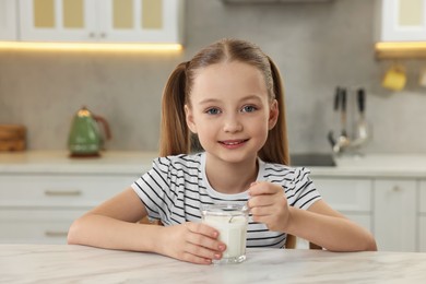 Cute little girl with tasty yogurt at white marble table in kitchen