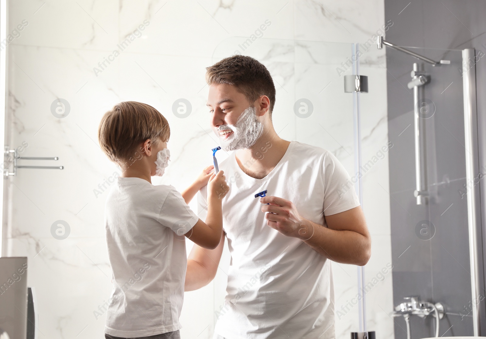 Photo of Dad and son with shaving foam on their faces having fun in bathroom