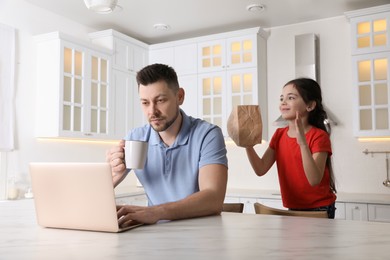 Photo of Cute little girl popping paper bag behind father's back while he working at home