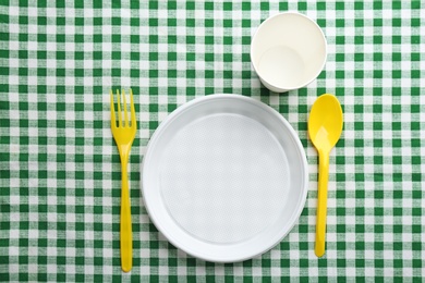 Composition with plastic dishware on checkered tablecloth, top view. Picnic table setting