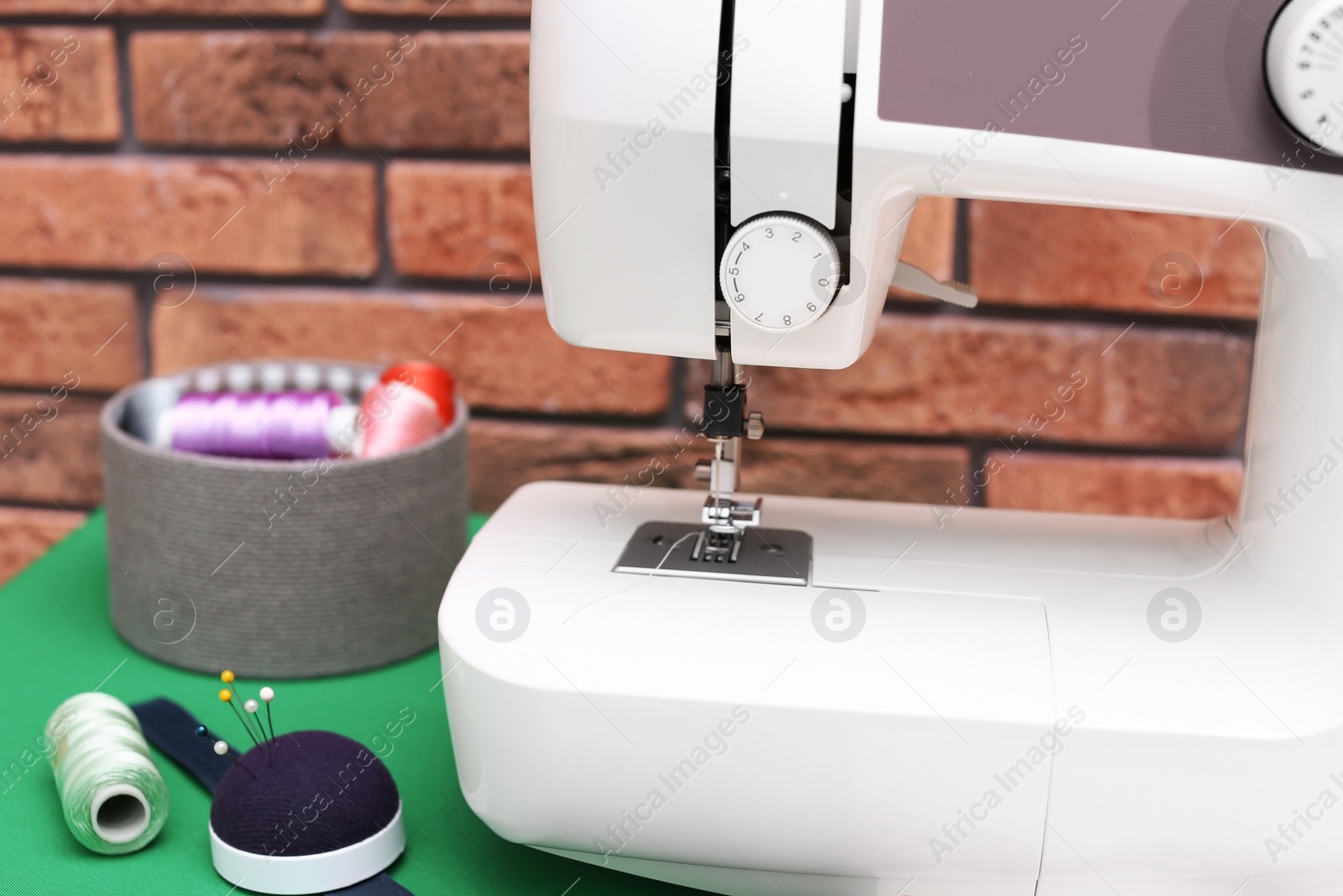 Photo of Modern sewing machine near brick wall, closeup