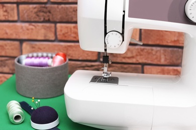 Photo of Modern sewing machine near brick wall, closeup