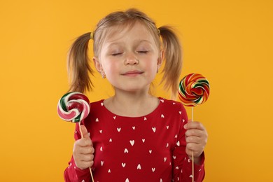 Photo of Cute girl with lollipops on orange background