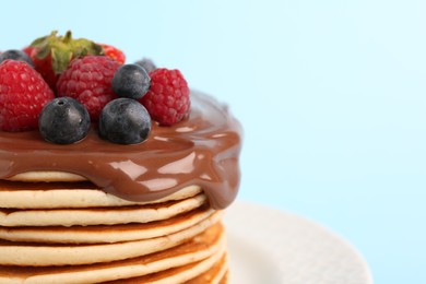 Photo of Stack of tasty pancakes with fresh berries and chocolate spread on light blue background, closeup. Space for text