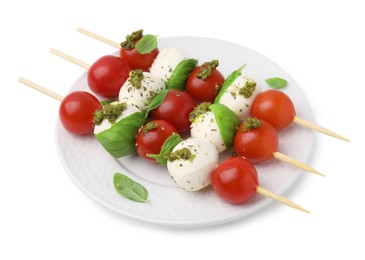 Photo of Plate of Caprese skewers with tomatoes, mozzarella balls, basil and pesto sauce isolated on white