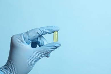 Photo of Doctor holding pill on light blue background, closeup. Space for text