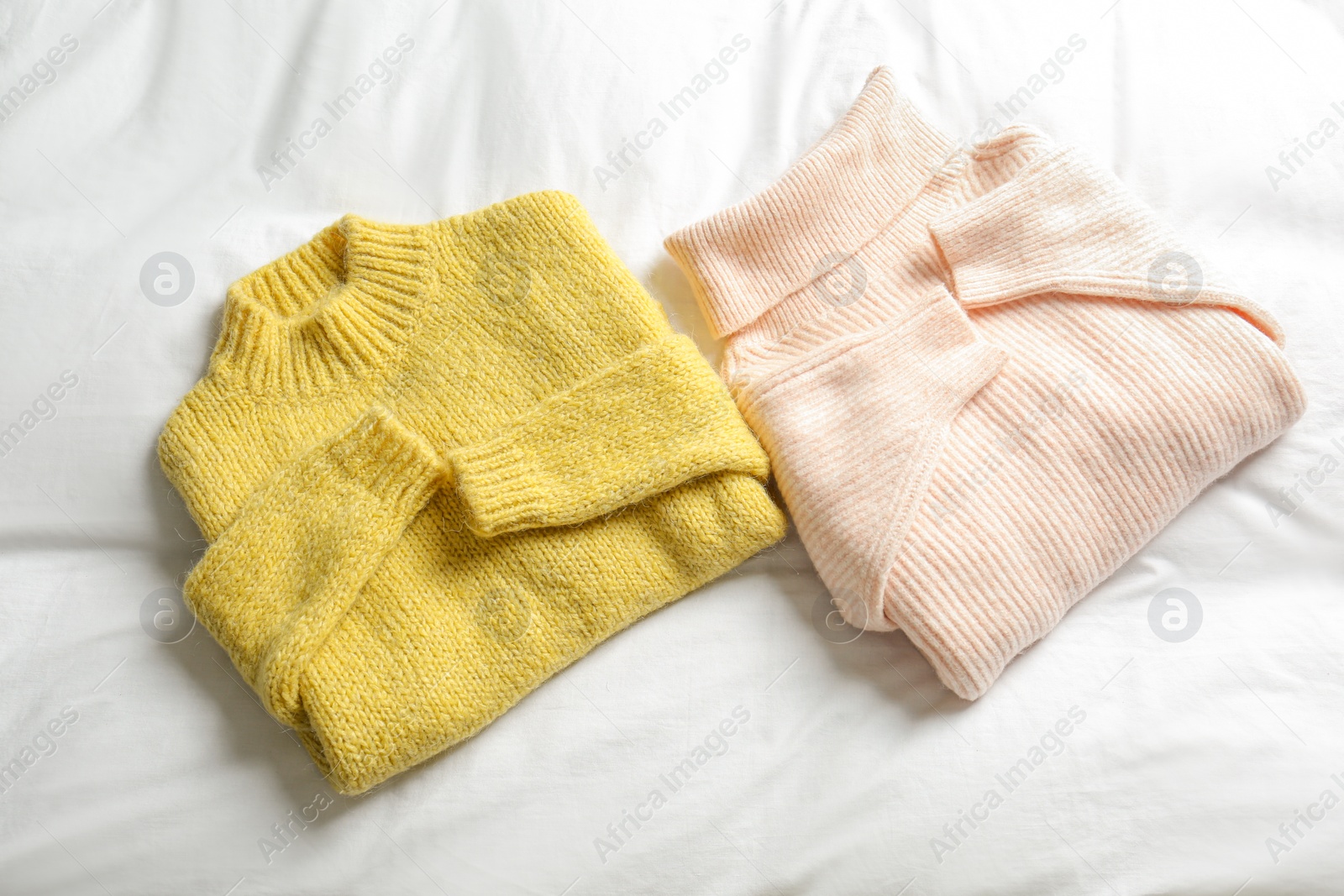 Photo of Stylish knitted sweaters on white fabric, flat lay