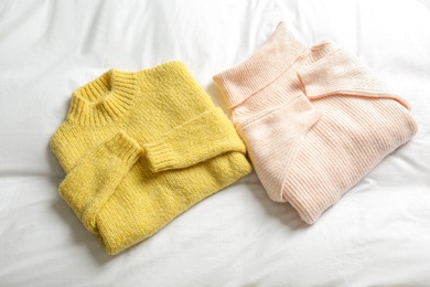 Stylish knitted sweaters on white fabric, flat lay