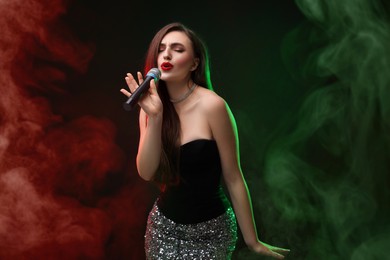 Image of Beautiful woman with microphone singing on stage in color lighted smoke