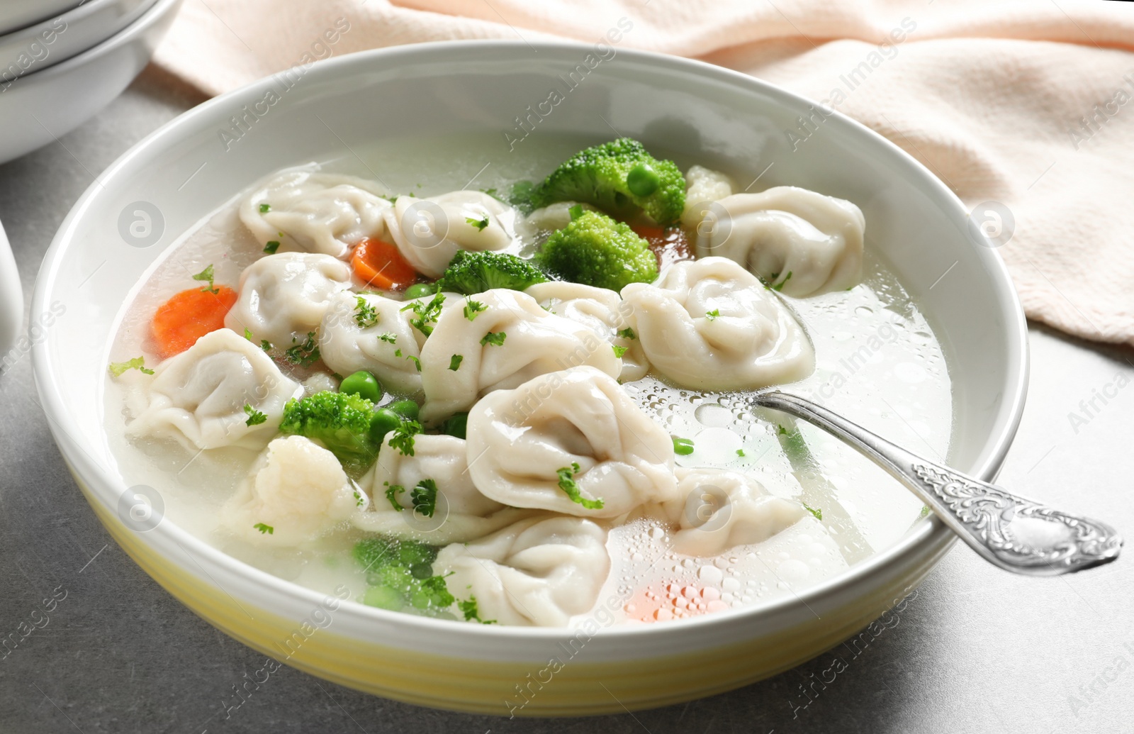 Photo of Bowl of tasty dumplings in broth with spoon on table, closeup