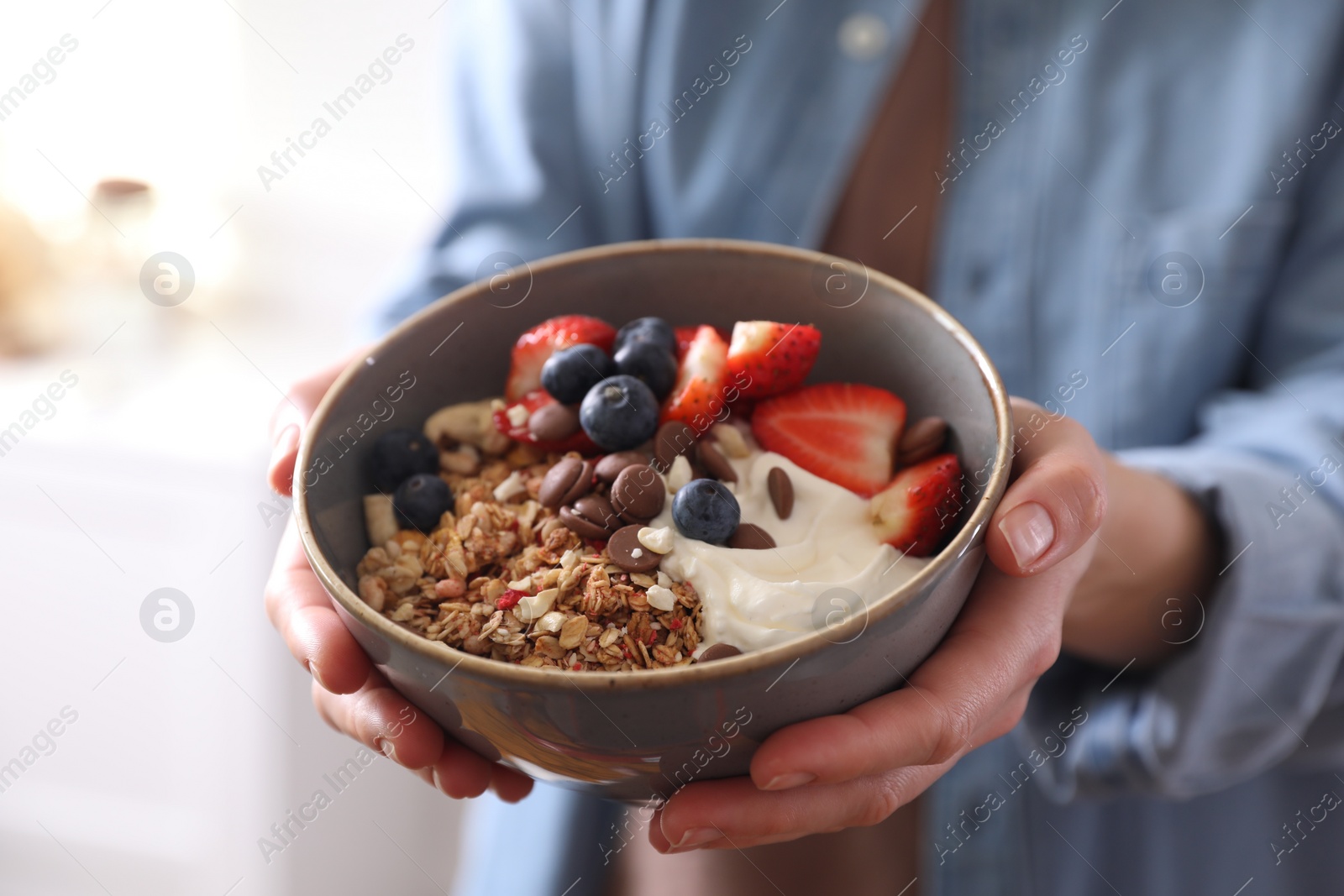 Photo of Woman holding bowl of tasty granola on blurred background, closeup