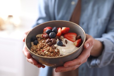 Woman holding bowl of tasty granola on blurred background, closeup