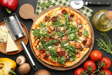 Photo of Delicious vegetarian pizza, ingredients, cutter and grater on black table, flat lay