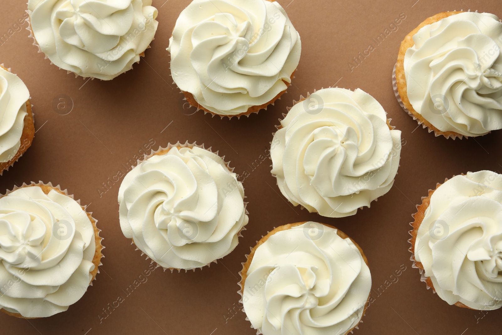 Photo of Tasty vanilla cupcakes with cream on dark beige background, top view