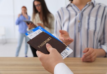 Agent giving passport with ticket to client at check-in desk in airport, closeup