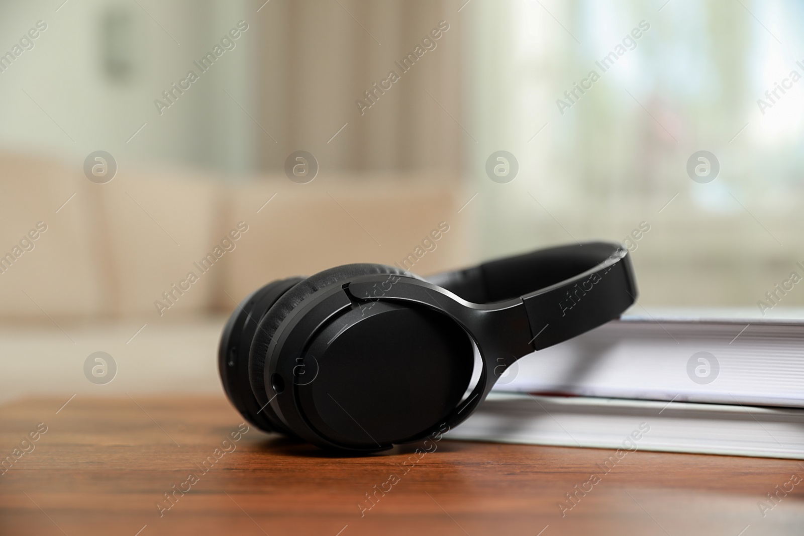 Photo of Modern wireless headphones and books on wooden table indoors