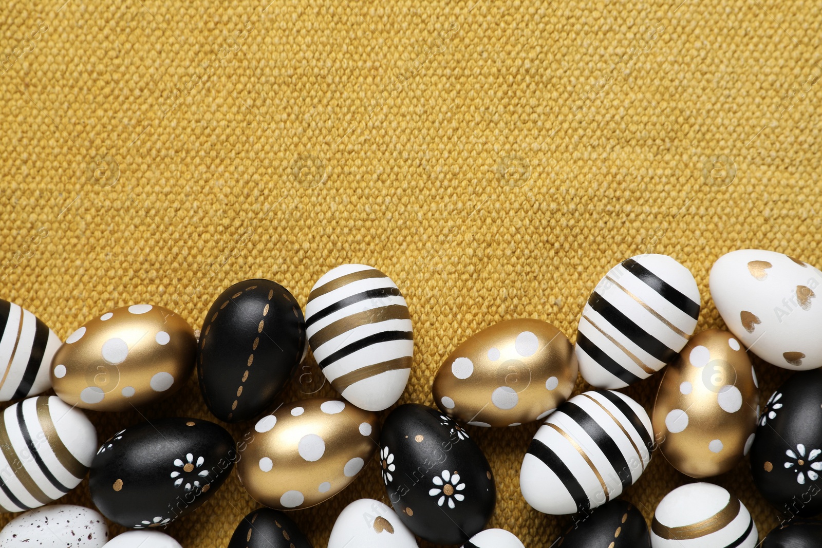 Photo of Many beautifully decorated Easter eggs on yellow fabric, flat lay. Space for text