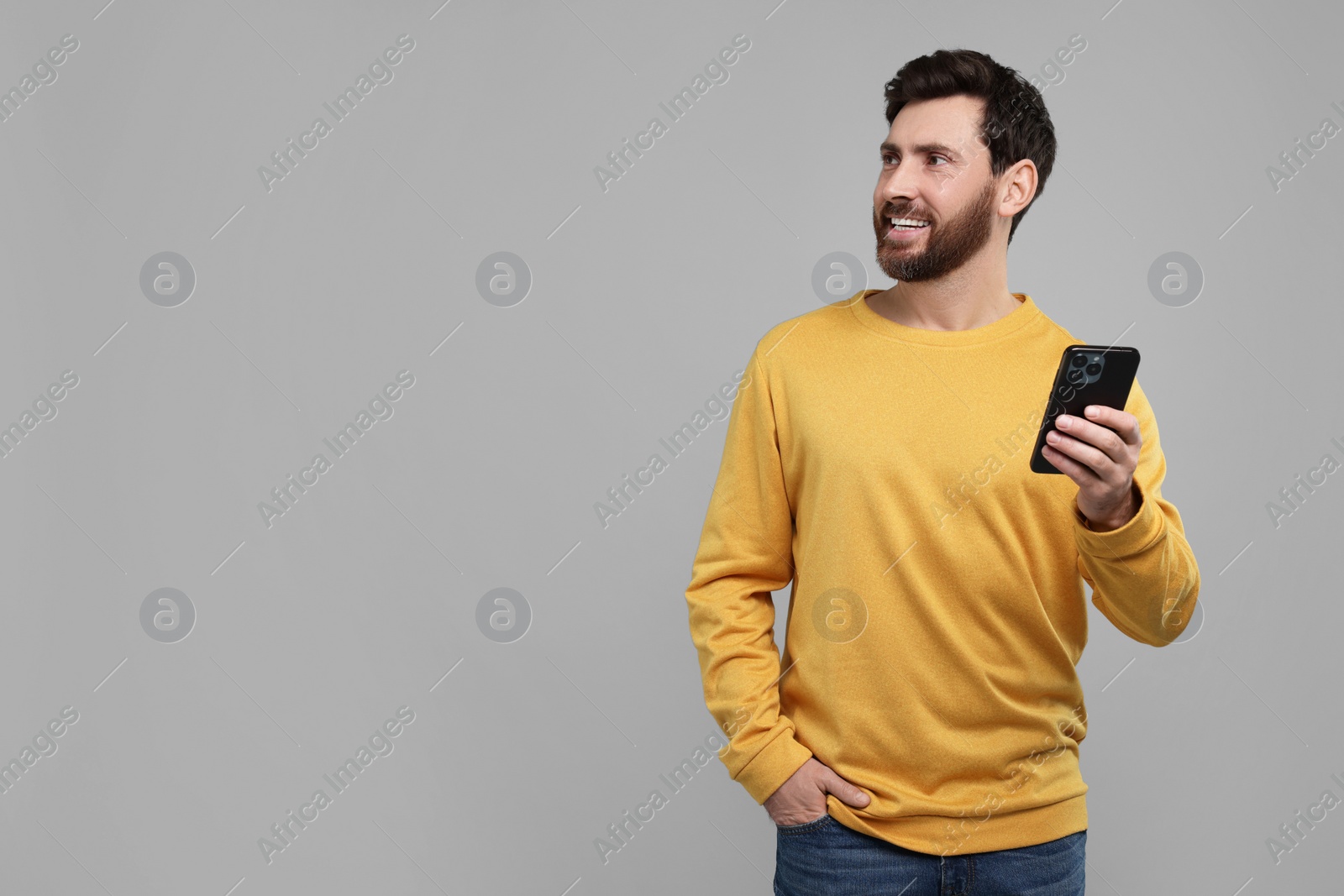 Photo of Smiling man with smartphone on grey background. Space for text