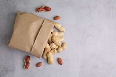 Paper bag with fresh unpeeled peanuts on grey table, top view. Space for text