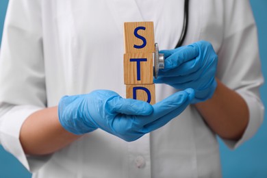 Photo of Doctor holding wooden cubes with abbreviation STD and stethoscope on light blue background, closeup