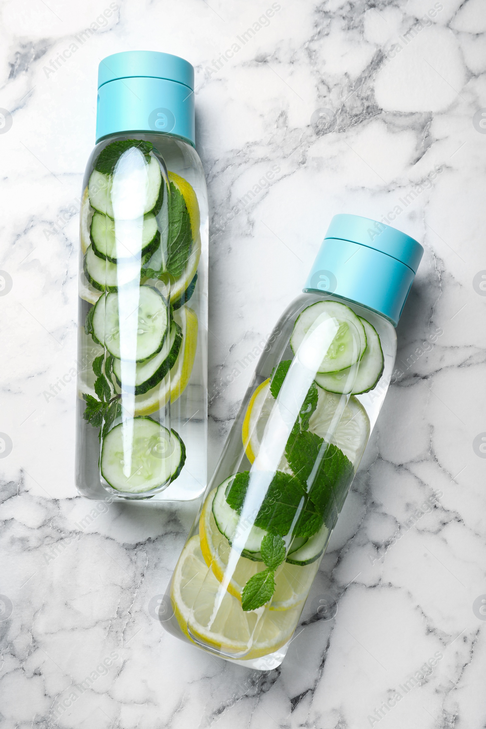 Photo of Bottles of refreshing water with cucumber, lemon and mint on white marble table, flat lay