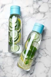 Bottles of refreshing water with cucumber, lemon and mint on white marble table, flat lay