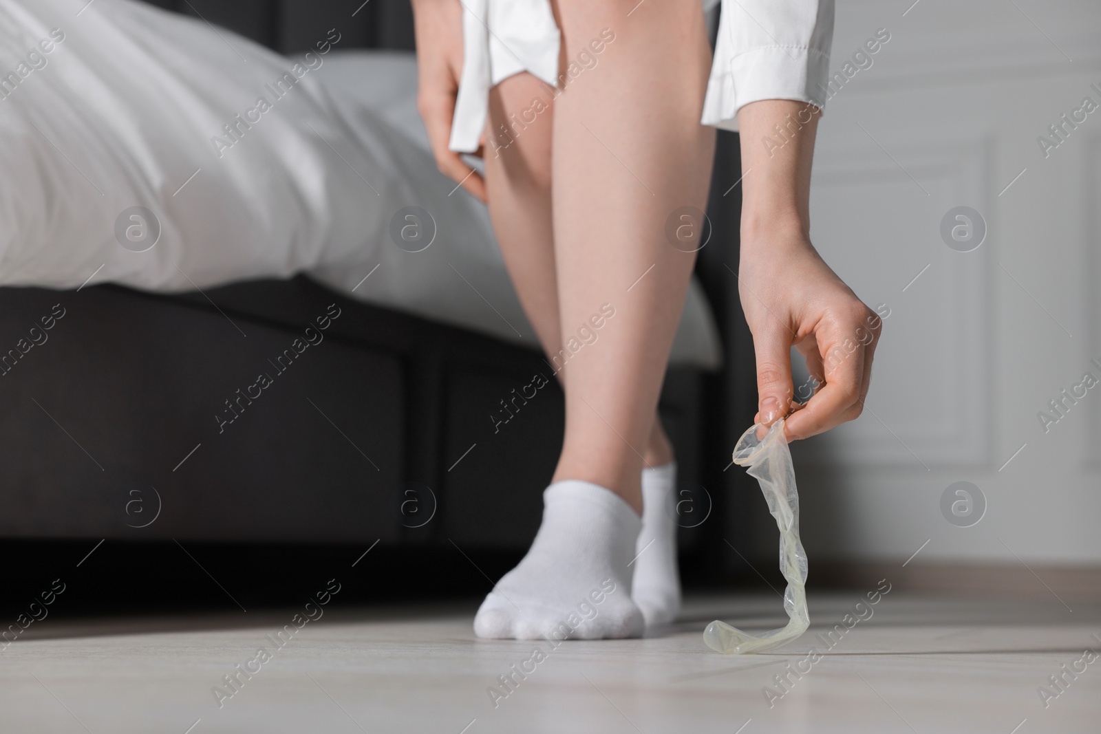 Photo of Woman taking unrolled condom from floor indoors, closeup. Safe sex