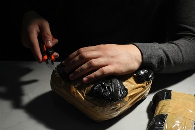 Photo of Smuggling and drug trafficking. Man opening package of narcotics with box cutter in darkness, closeup