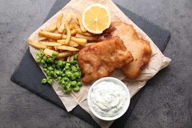 Photo of Tasty fish, chips, sauce and peas on grey table, top view