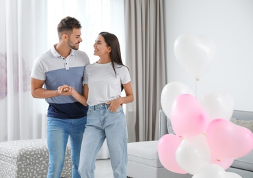 Photo of Young couple in living room decorated with air balloons. Celebration of Saint Valentine's Day