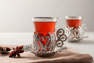 Photo of Glasses of traditional Turkish tea in vintage holders and anise stars on table, closeup