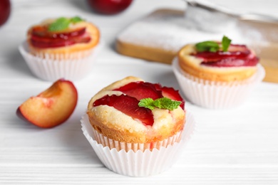 Photo of Delicious cupcakes with plums on white wooden table, closeup