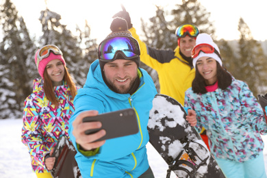 Photo of Group of friends taking selfie on snowy hill. Winter vacation