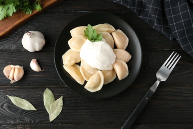 Photo of Delicious cooked dumplings with sour cream on dark wooden table, flat lay